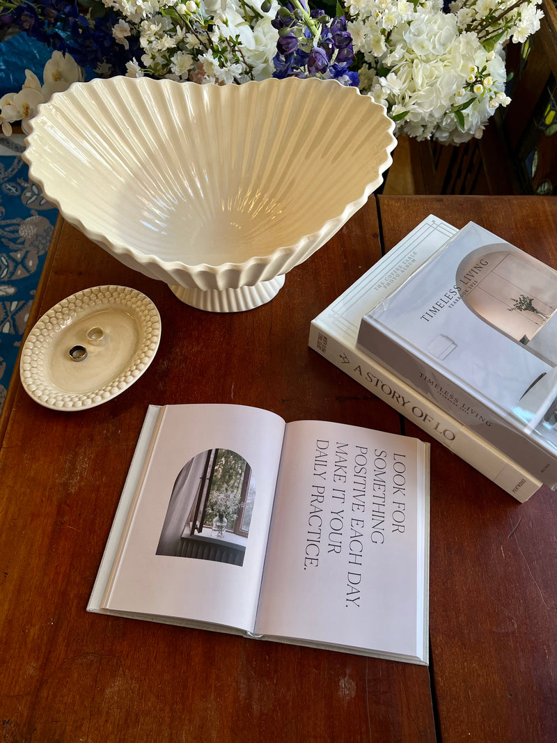 Ivory white decorative bowl from Ferm Living looks so good with the Bubbles oval dish by Mateus on a wooden table with an open book from Cozy publishing and stack of other interior design books.