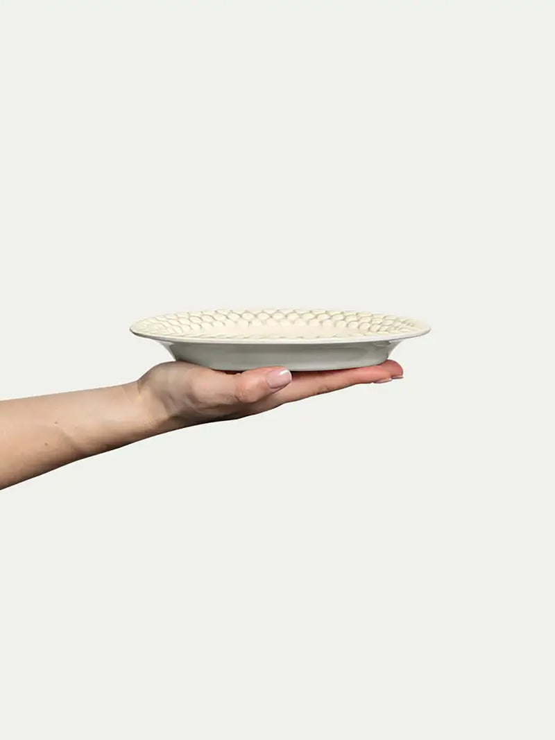 Hand holding a ceramic plate with a textured pattern on a white background