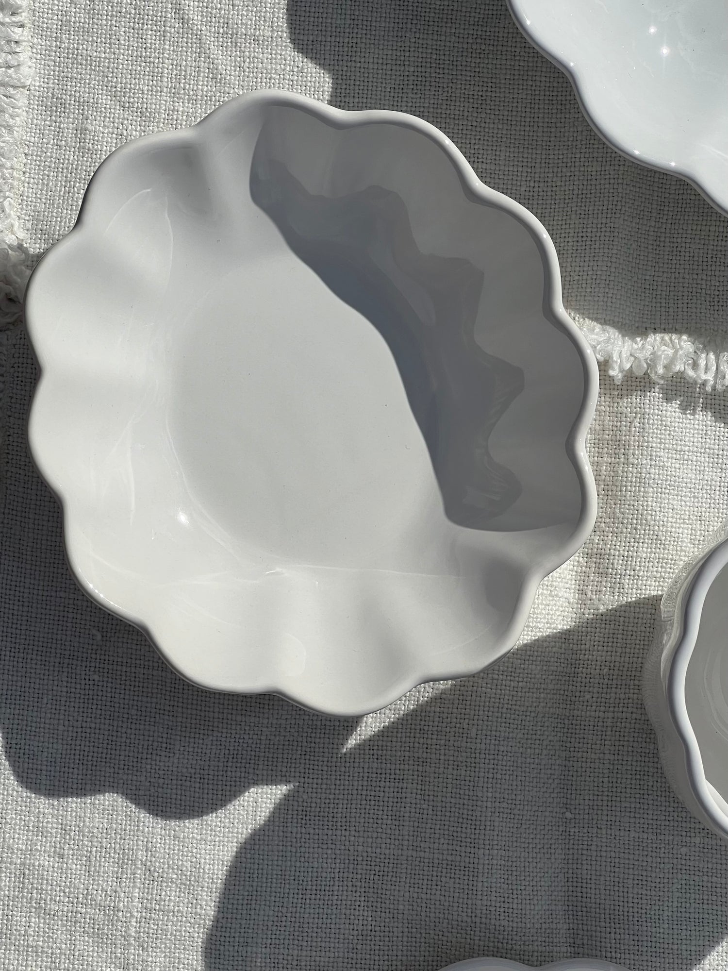 White ceramic bowl with scalloped edge on a textured surface