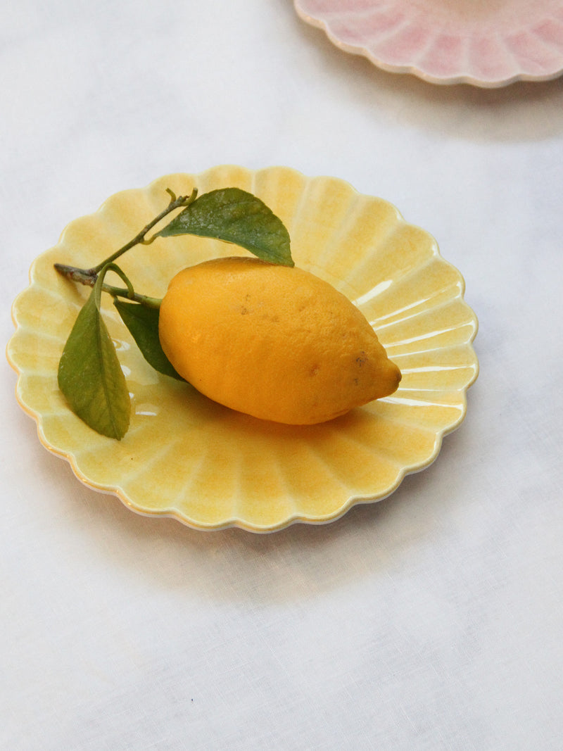 The small Oyster yellow ceramic plate fits  a big lemon, shown here on a light tablecloth with the small Oyster light pink ceramic plate on the backround.