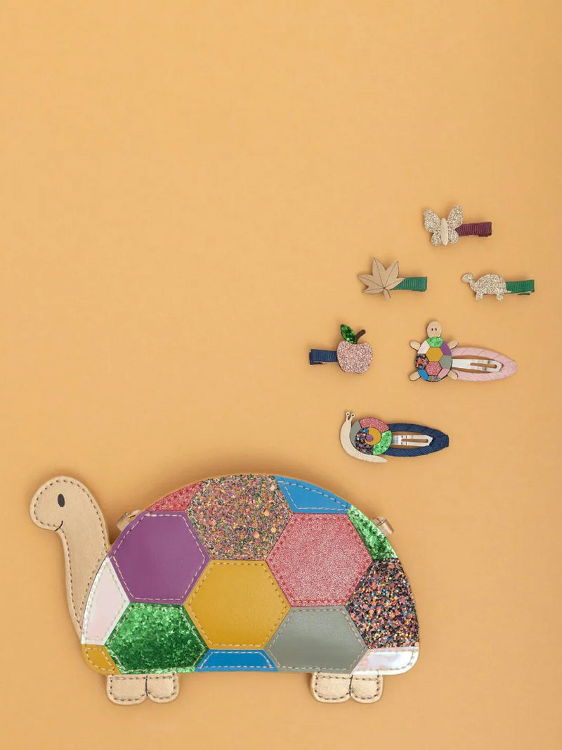 Colorful tortoise-shaped bag with decorative hair clips on a beige background