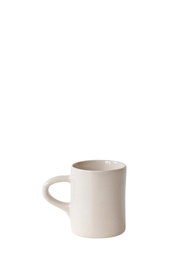 A minimalist ceramic mug with a well-proportioned handle in a warm off-white or cream solid colour with glossy glaze finish, positioned in the lower half of a solid white picture.
