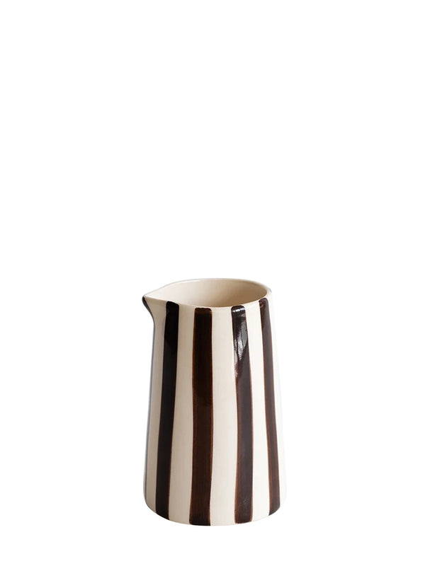 A conical ceramic pitcher with a glossy finish, featuring a small little pouring beak and handpainted vertical dark brown stripes on cream white base, set against a plain white background.