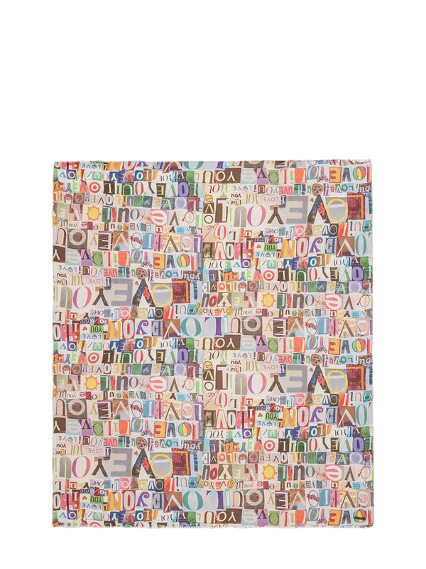 A square fabric item, likely a clutch cover or small pouch, featuring a dense multicolor collage pattern of the word 'AMERICA' in various fonts and colors on a light background.