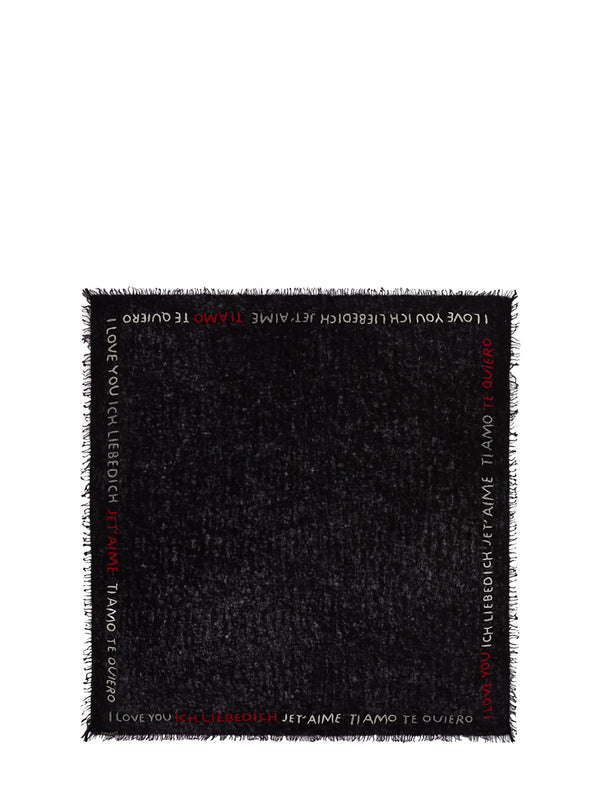 A black woven throw blanket with fringe edges, featuring white and red text printed along the borders.