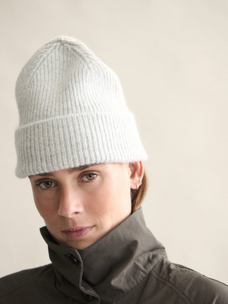 Person wearing a light gray knit beanie and dark jacket against a plain background