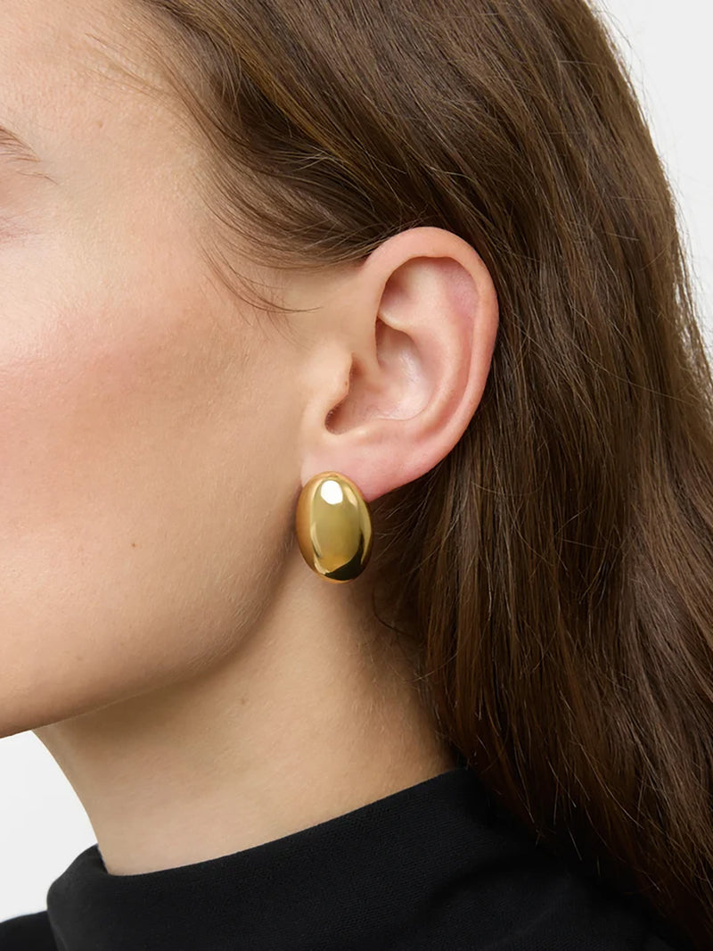 A close-up of a model's ear, jawline, hair and neck wearing a medium-sized polished, oval-shaped gold earring.