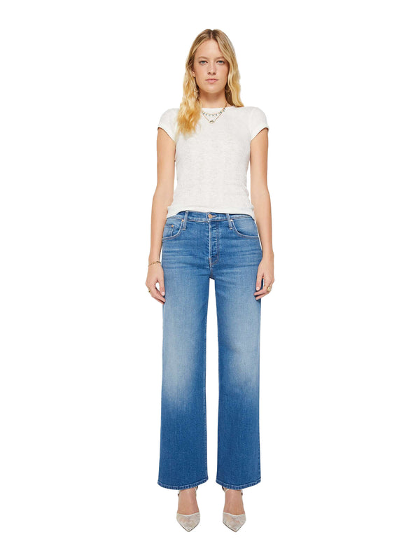 A woman modeling a pair of wide-leg blue jeans with a faded wash, paired with a white short-sleeve top and pointed nude heels, set against a plain white background.