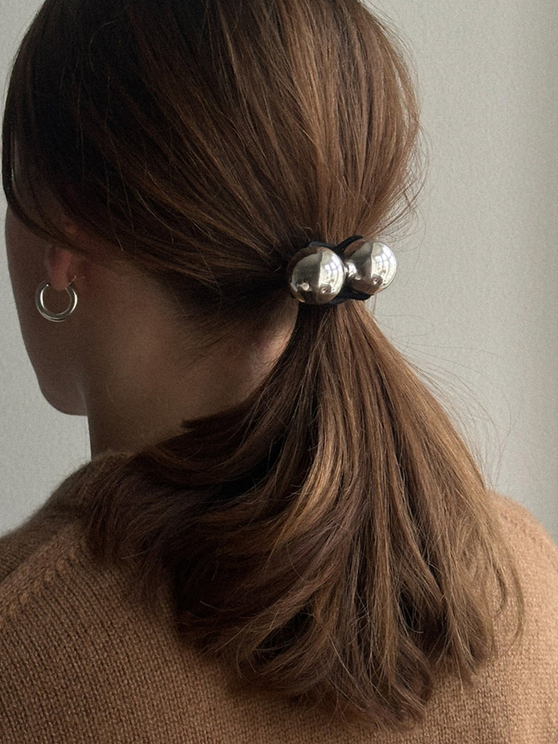 Person with a ponytail held by a hair tie with silver beads against a neutral background