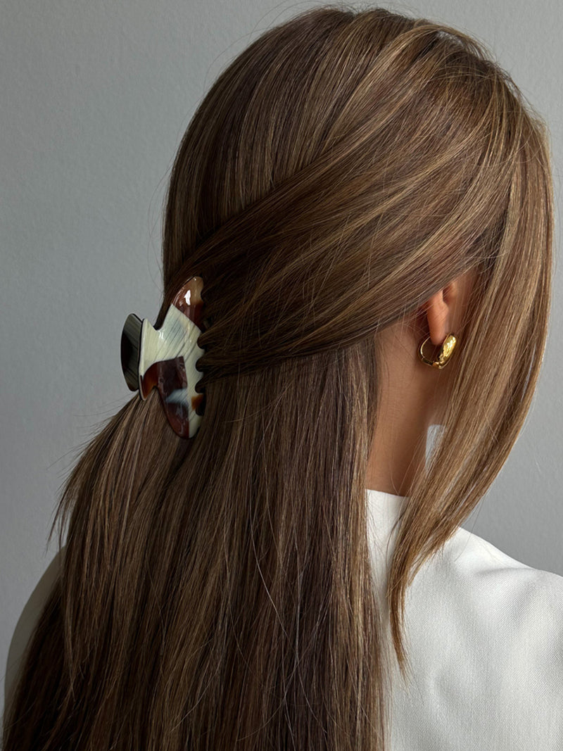 Person with a ponytail using a decorative hair tie against a neutral background