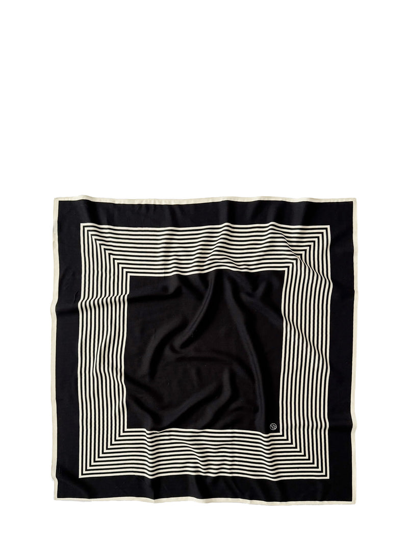 A square black scarf with a cream-colored border and concentric striped geometric pattern, laid flat on a white background.