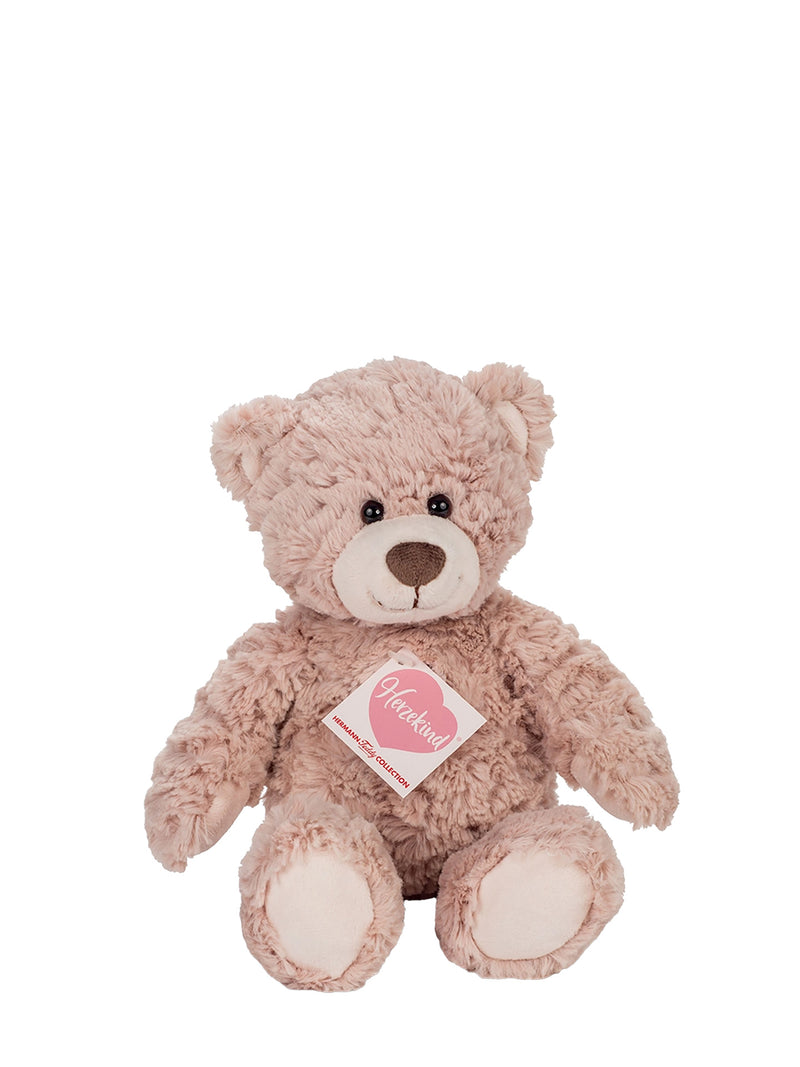 A light pink plush teddy bear with a white snout and black eyes, sitting against a plain white background. A pink tag with a heart and the word 'Huggable' is attached to its chest.