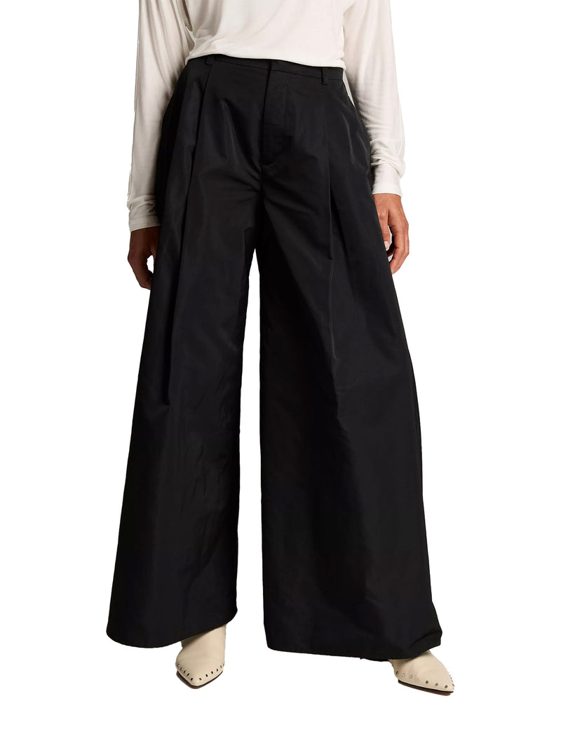 A model wearing black wide-leg pleated trousers, styled with a cream long-sleeve top and cream pointed-toe flats, shown from the waist down on a white background.