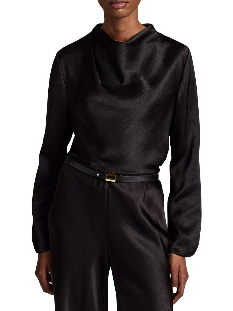 A model wearing a black long-sleeve satin mock neck top and matching black satin trousers, styled with a black belt with a gold buckle, against a plain white background.