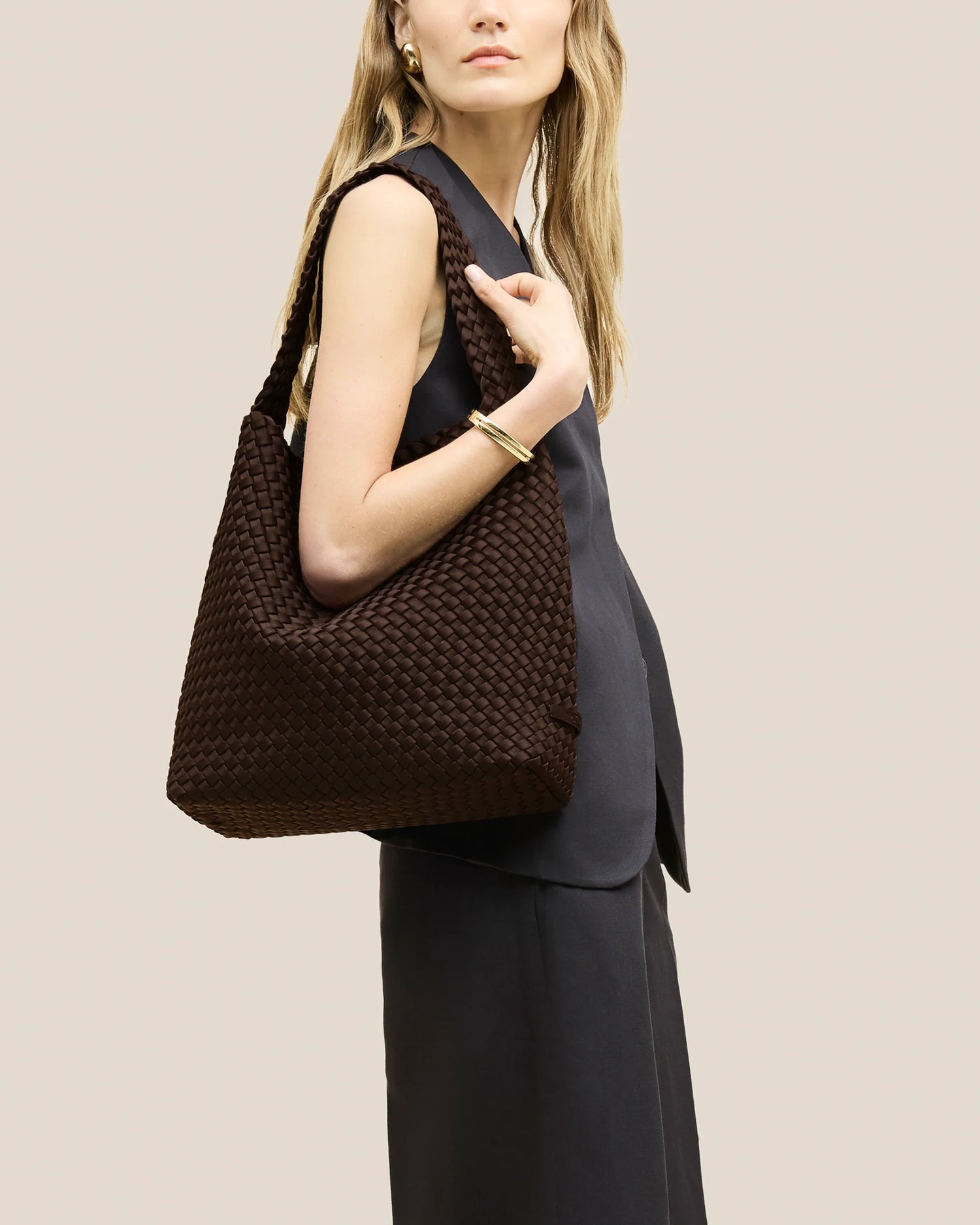 Woman holding a brown woven handbag against a beige background