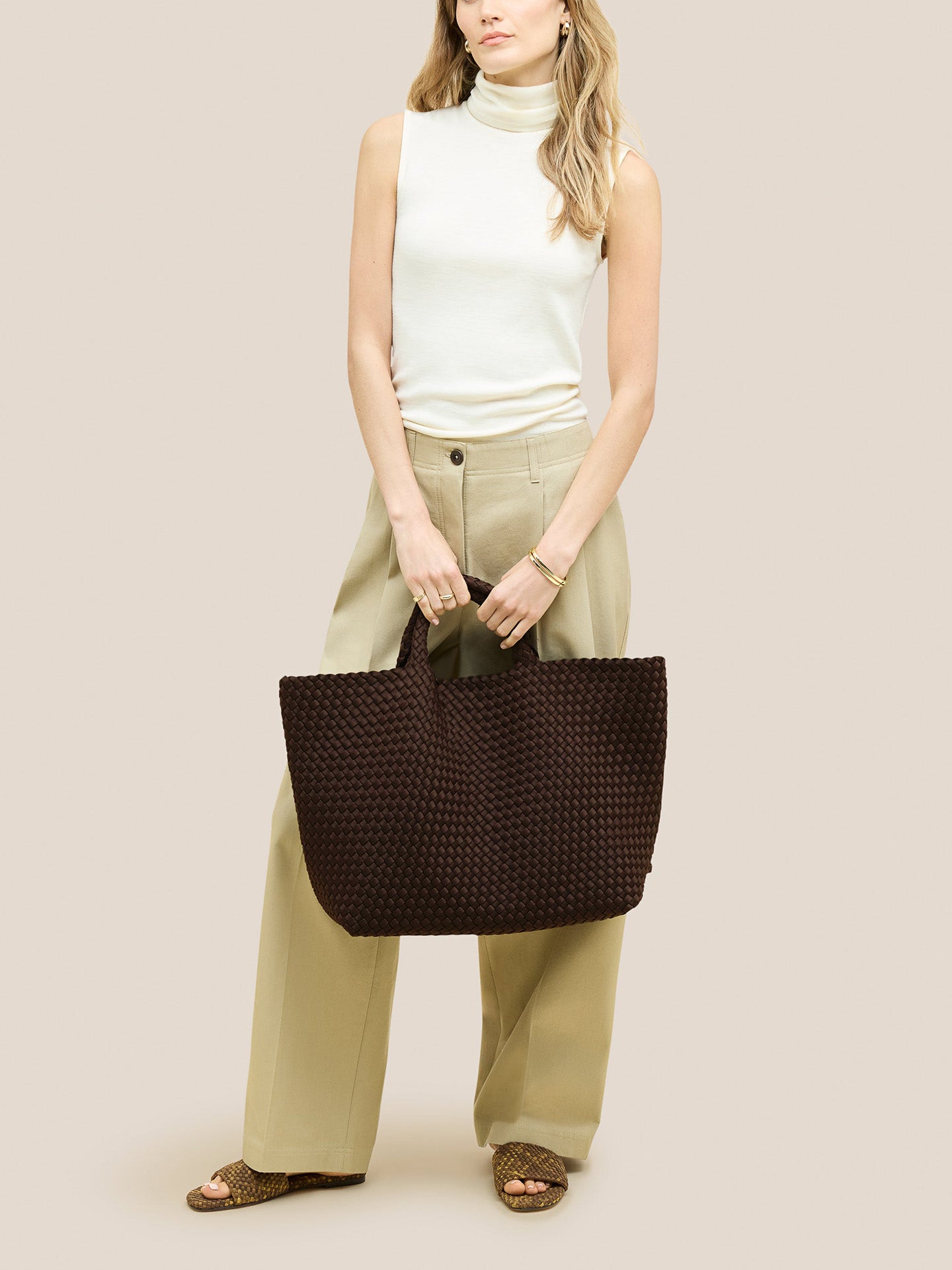 Woman holding a brown woven handbag against a plain background