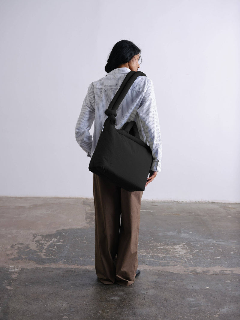 Person holding a large soft-looking black bag on their shoulder against a plain background