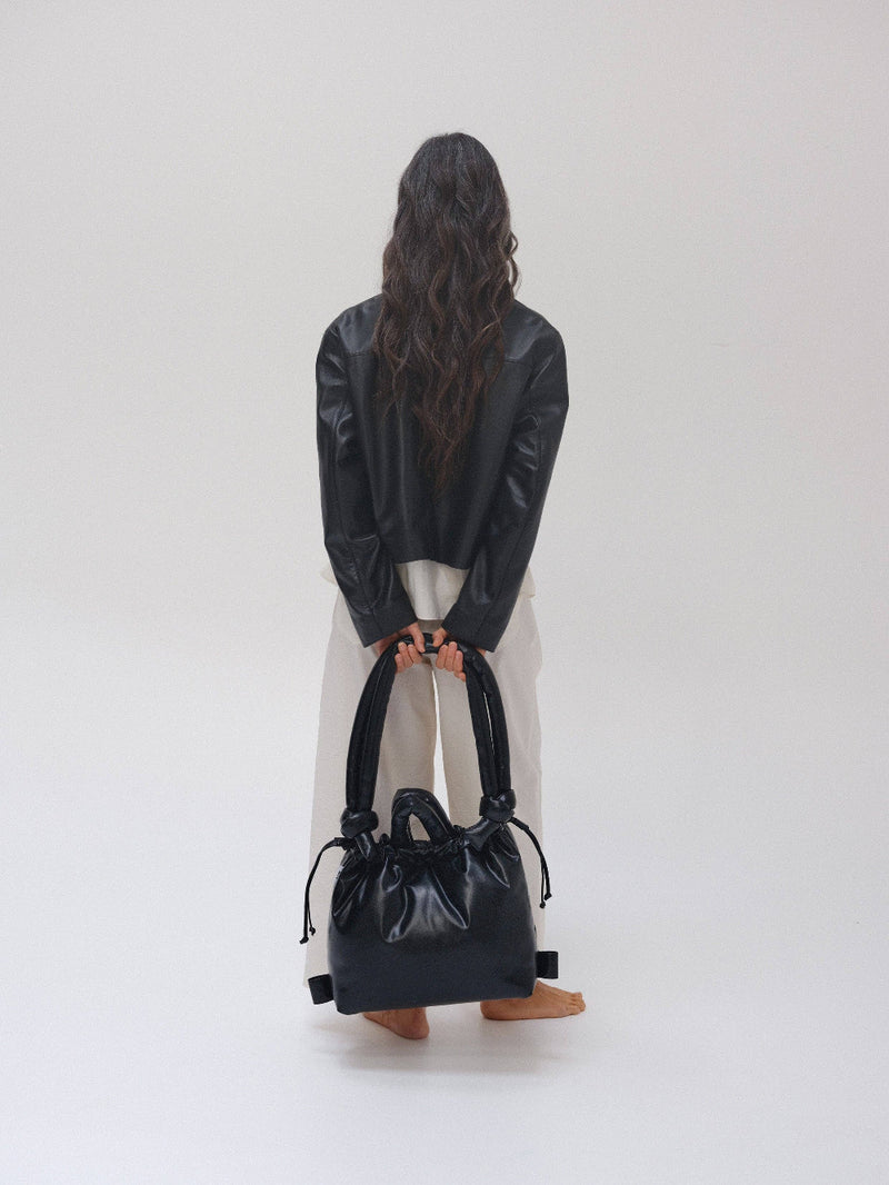 Person holding a black leather tote bag or carryall against a white background