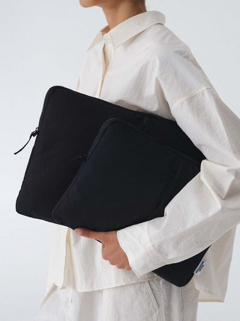 Person holding two black nylon laptop cases with visible black zippers at their upper third, and a small black zipper pulley against a white background