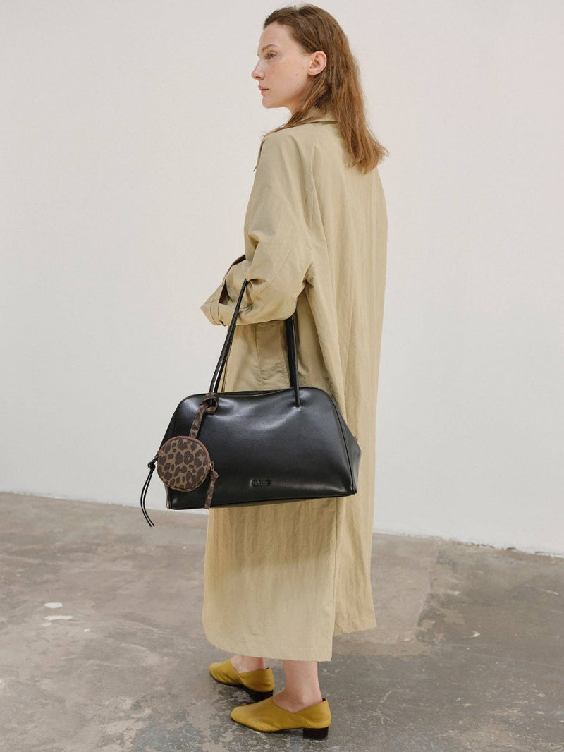 Woman holding a black handbag with a leopard print detail against a plain background
