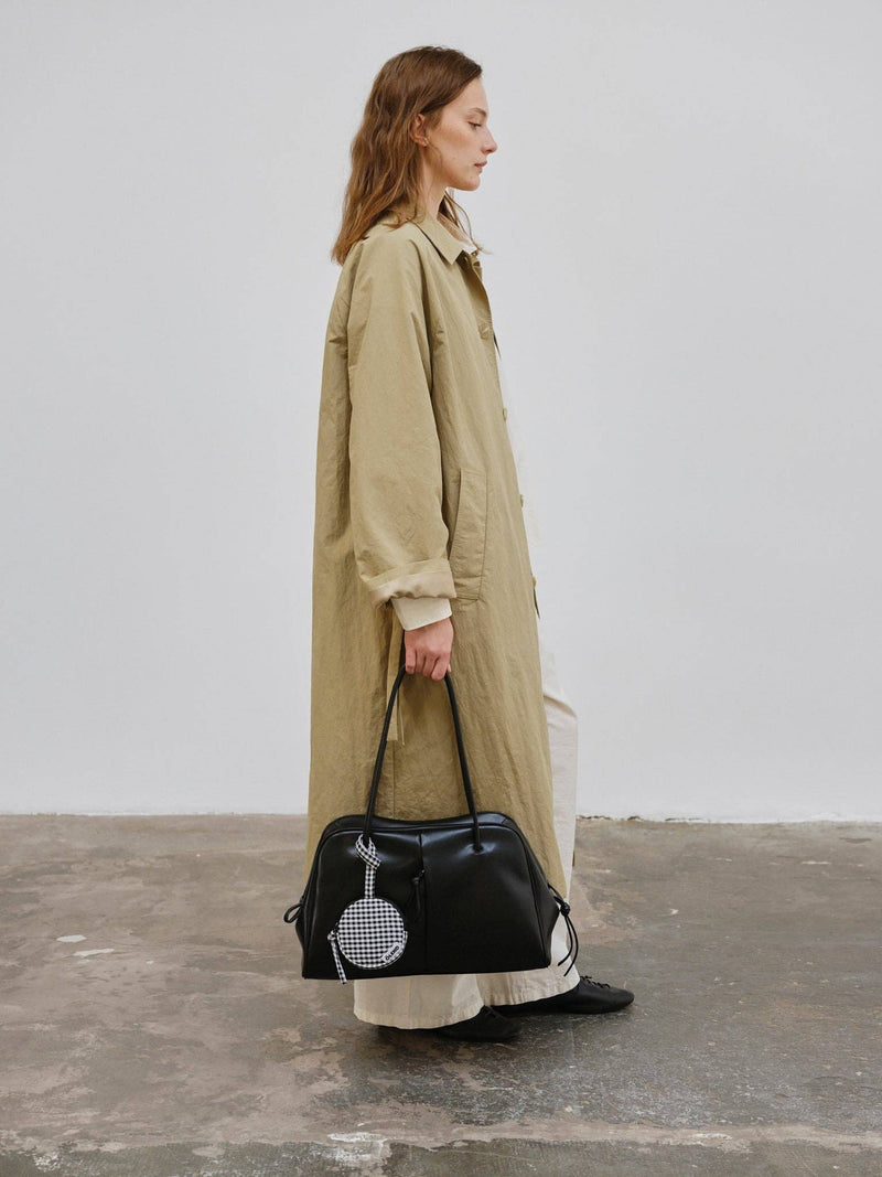 Woman in a long beige coat holding a black handbag with a white background