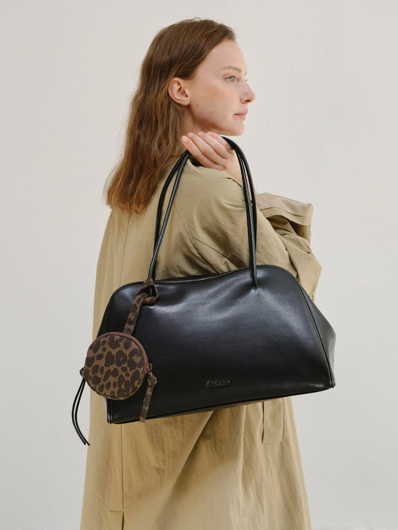 Woman holding a black handbag with a smaller round bag attached, on a plain background