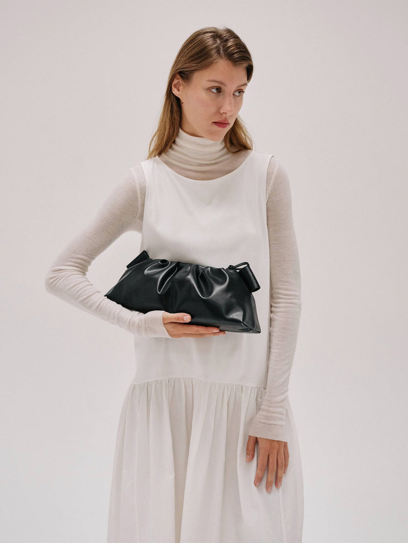 Woman holding a black clutch bag against a plain background