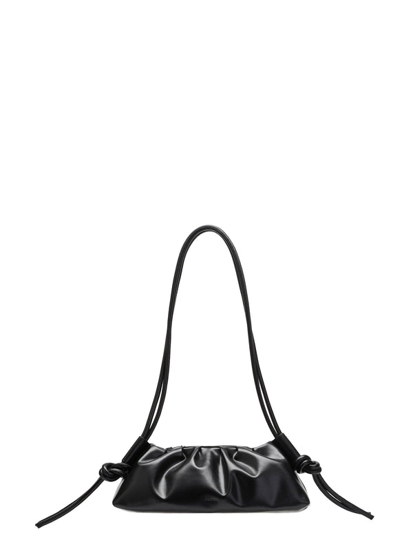 A black leather shoulder bag in with a gathered, slouchy baguette silhouette and a long, thin shoulder straps that attach in the bag body in a tube, then are knotted in a knot and are left hanging as cord ends, shown against a plain white background.