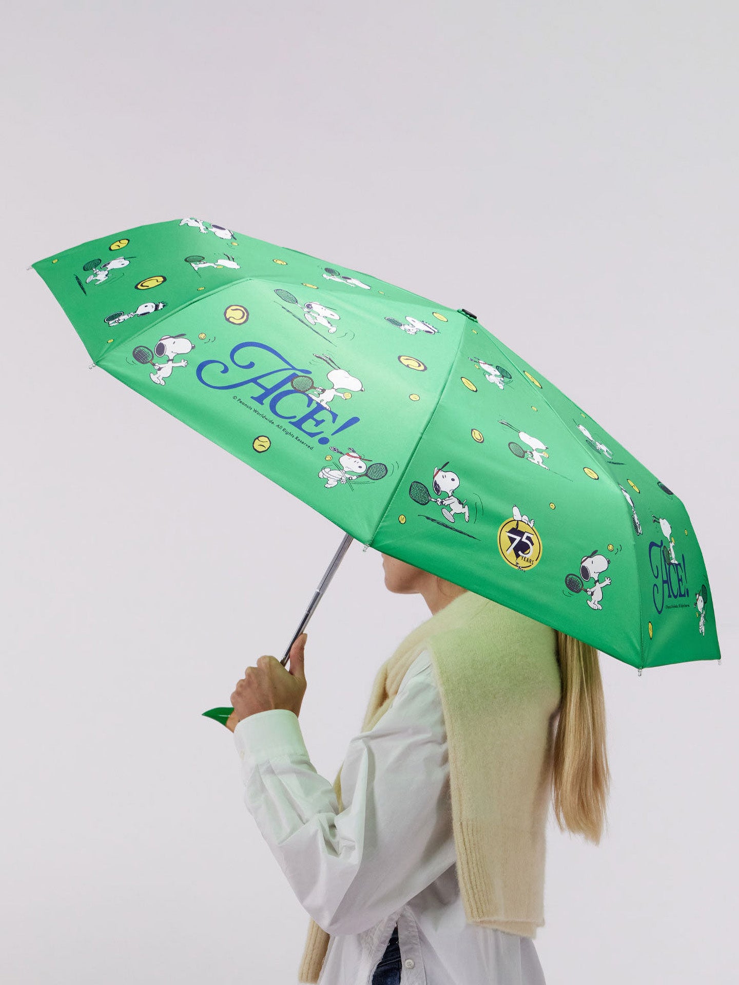 Person holding a green umbrella with Snoopy cartoon characters on a white background