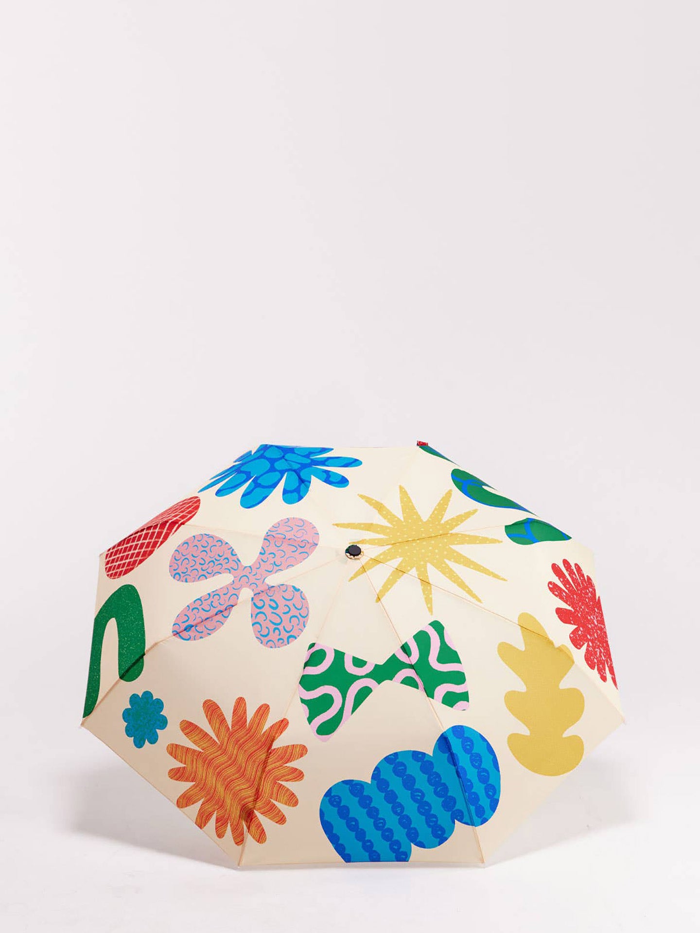 A cream-colored umbrella with a vibrant, multicolored retro floral and abstract pattern, photographed on a clean white studio background.