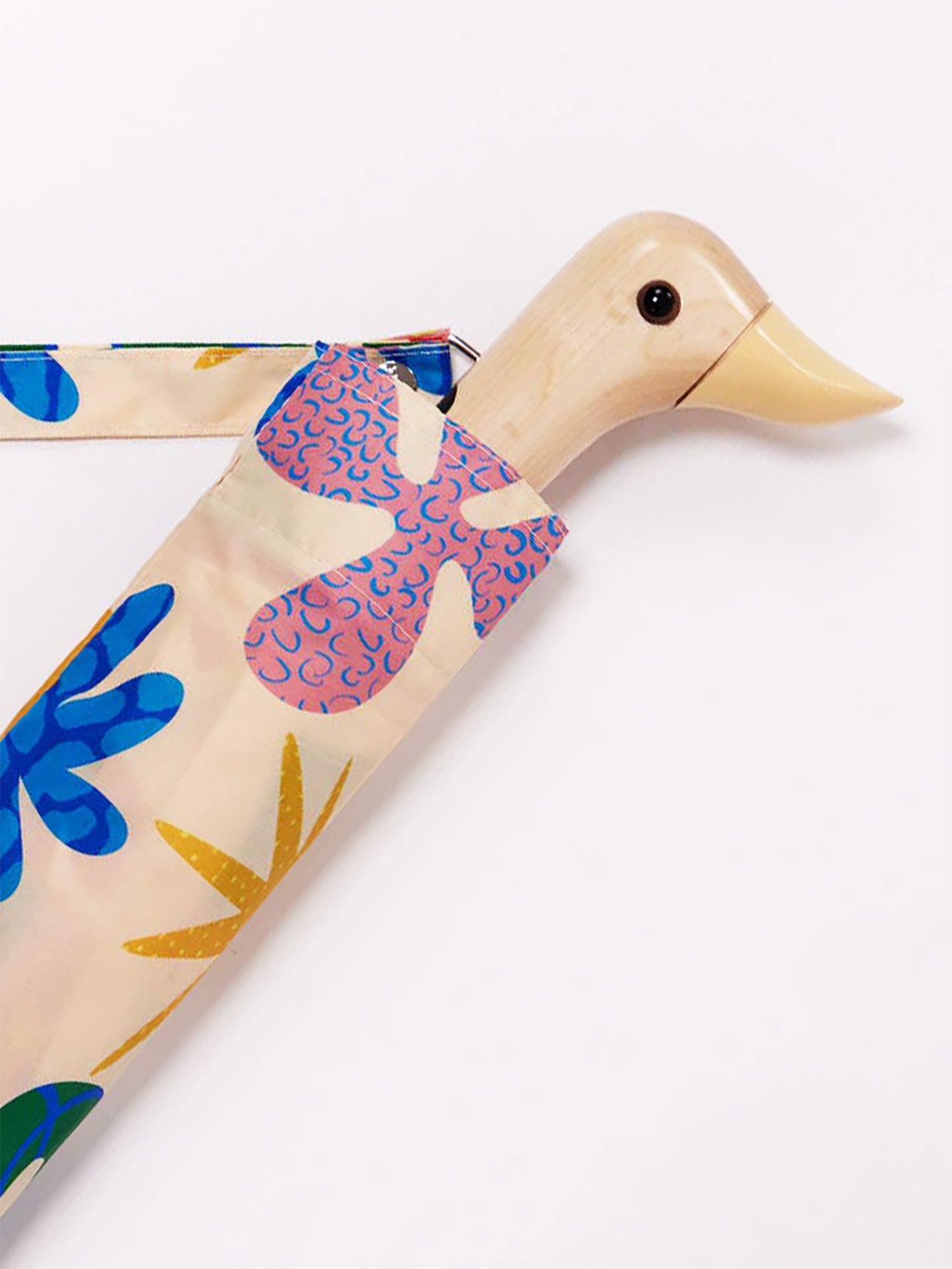A wooden duck-shaped umbrella handle with a beige body, light butter yellow beak, and black eye, partially covered by a patterned fabric sleeve in blue, pink, and yellow on a cream background, set against a plain white studio background.