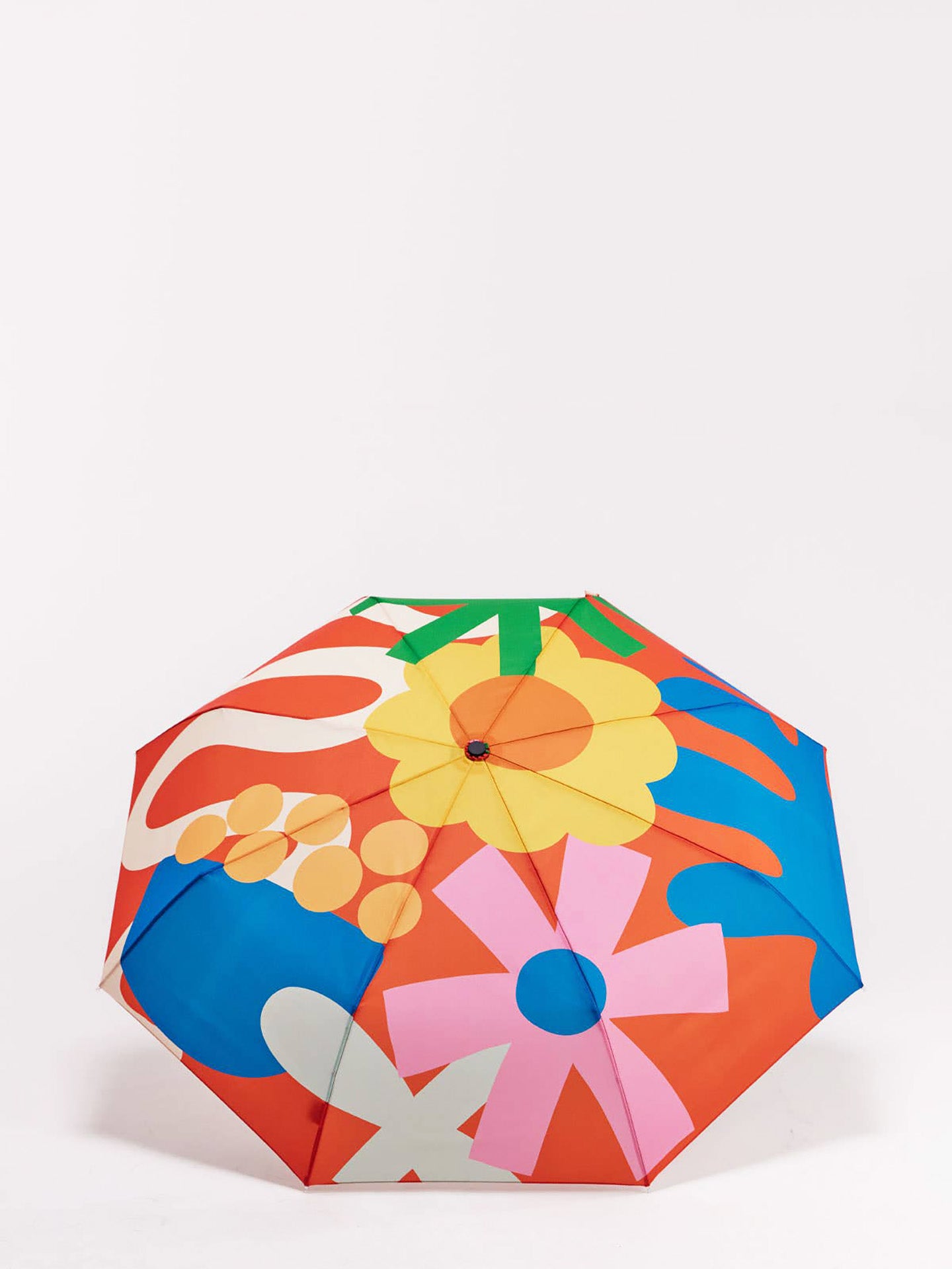 A compact umbrella with a bold retro floral and abstract pattern in orange, blue, pink, yellow, green, and white, photographed on a clean white background.