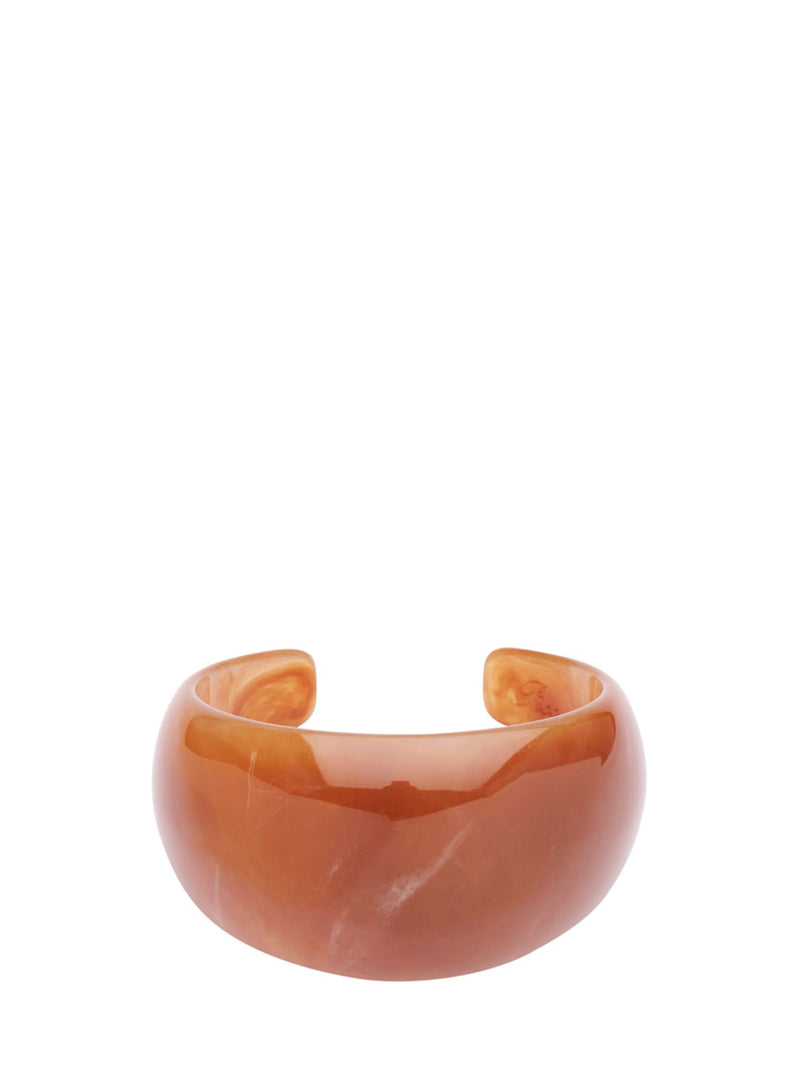 A wide, smooth open cuff bracelet made of glossy amber-brown resin or stone, photographed on a plain white background.