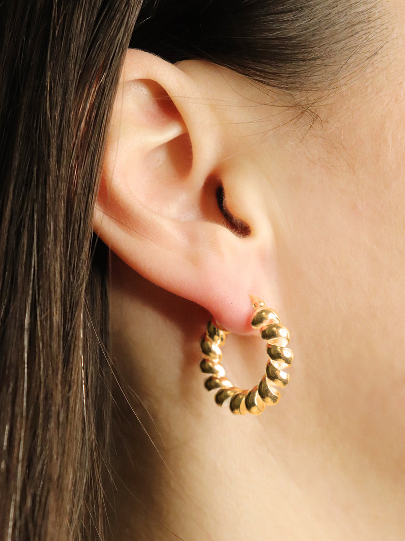 Gold hoop earring worn by a person with dark hair.
