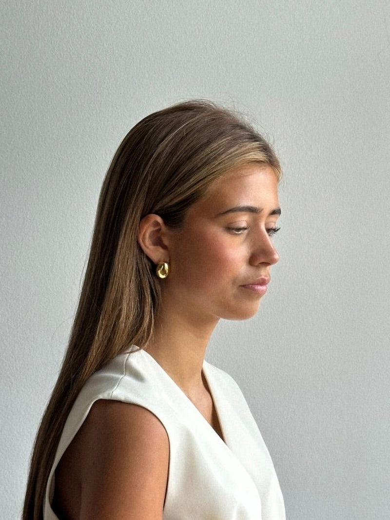 Woman wearing gold earrings against a plain background