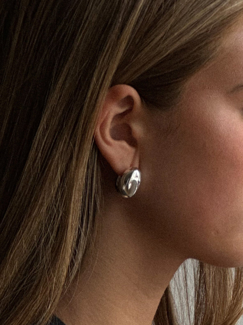 Close-up of a person wearing silver hoop earrings with a blurred background