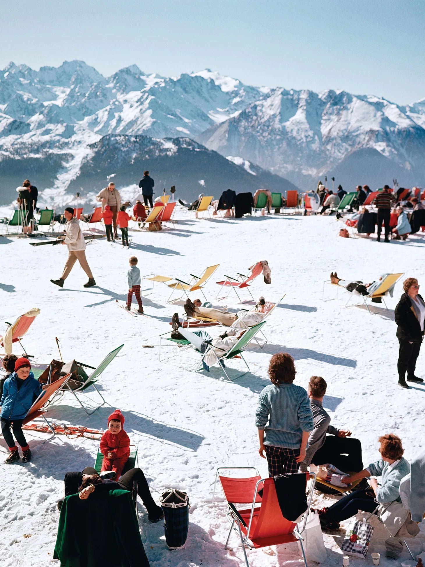 People relaxing on lounge chairs in the snow with mountains in the background