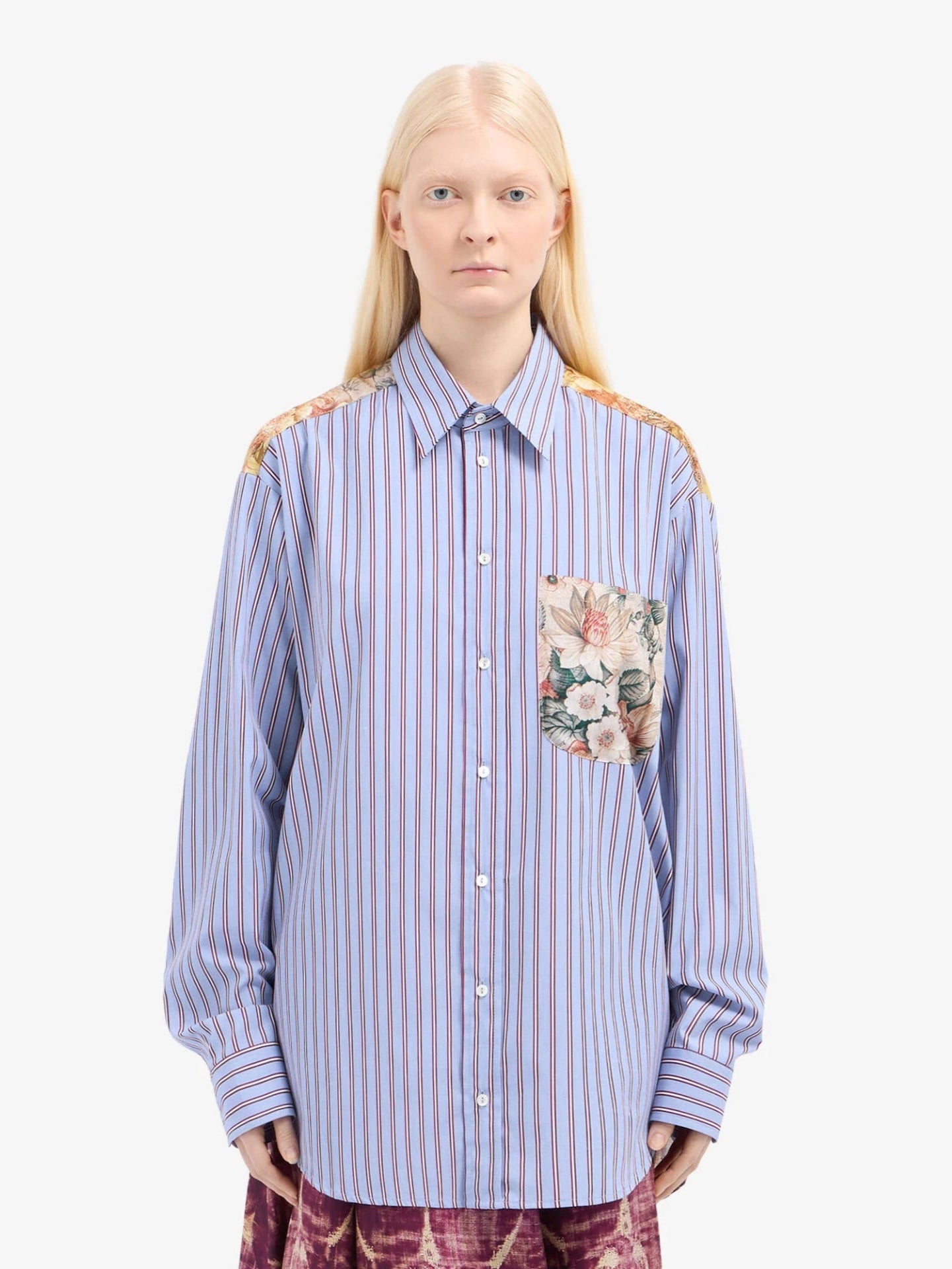 Person wearing a blue striped shirt with floral pocket on a white background