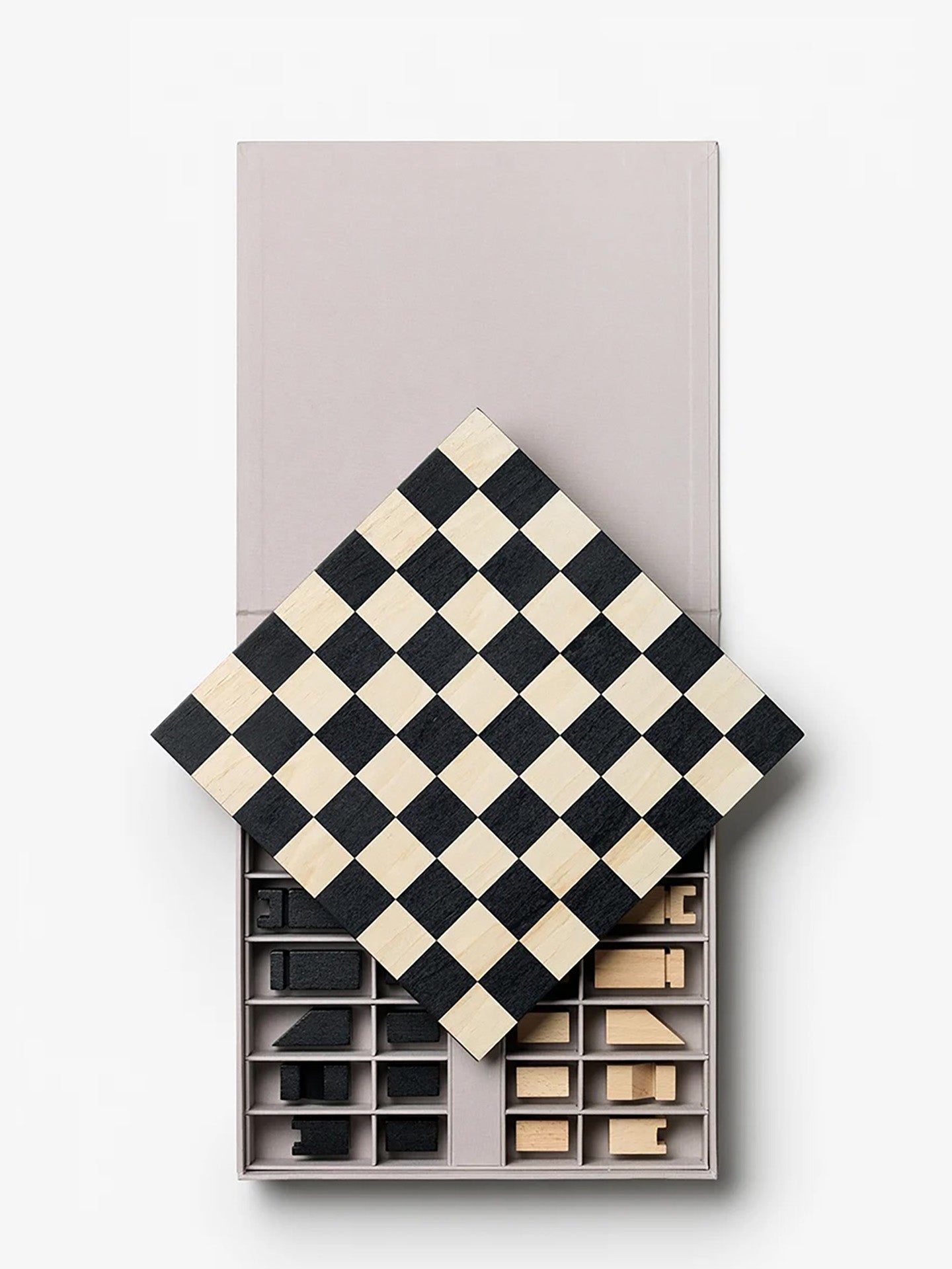 Wooden chess set in simple and clean design with a black and cream checkerboard lid resting over an open box containing wooden chess pieces, set against a plain white background.