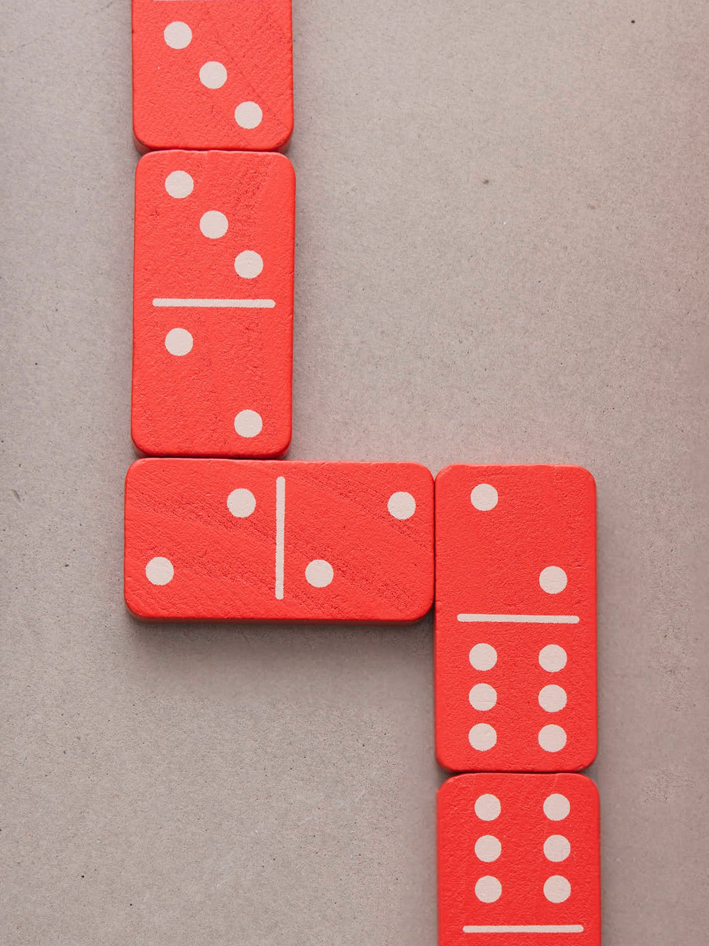 Red wooden domino tiles with white pips arranged in a turning line on a neutral gray background.