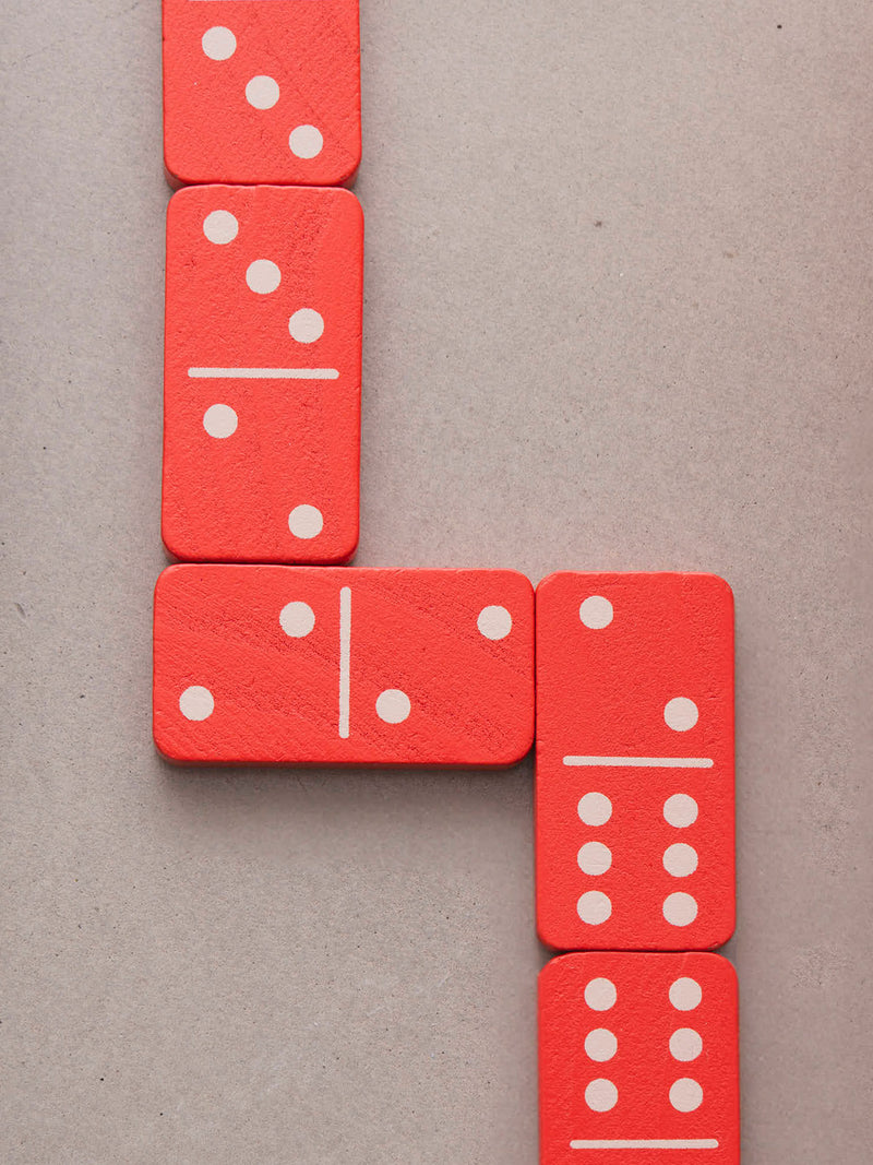 Red wooden domino tiles with white pips arranged in a turning line on a neutral gray background.