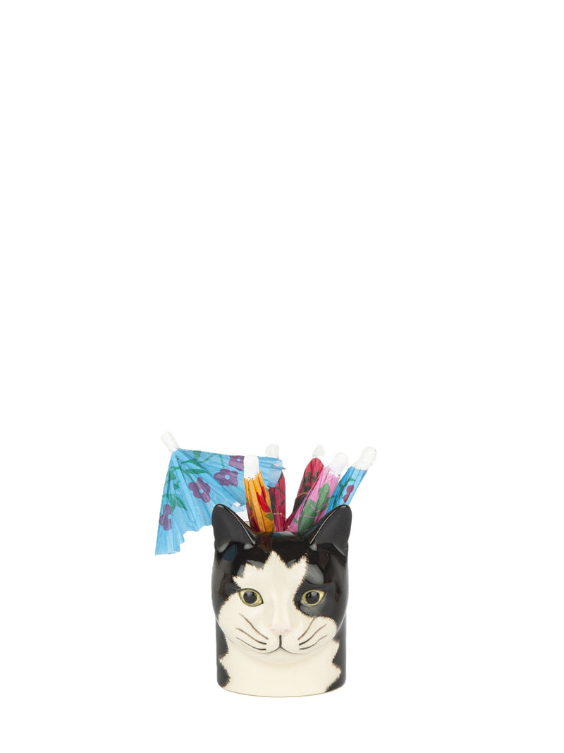 A novelty pen holder shaped like a black and white cat's face, holding several colorful pens and two small cocktail umbrellas, isolated on a white background.