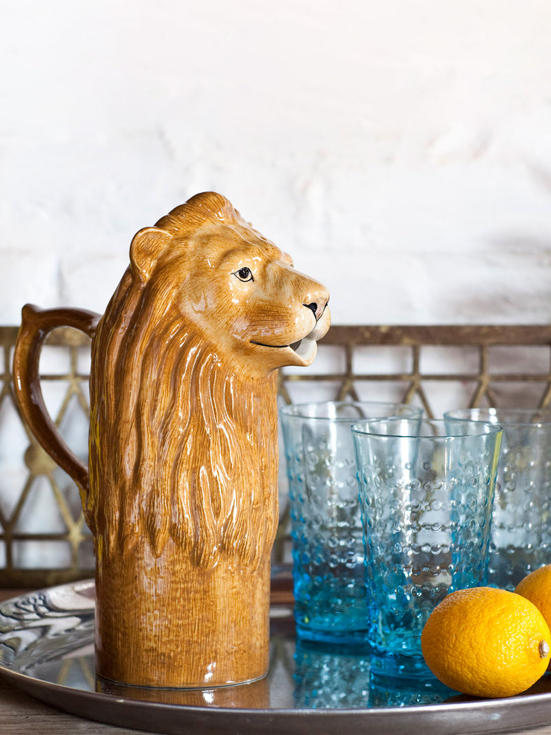 Lion-shaped ceramic pitcher on a tray with blue glasses and lemons ready to serve refreshing drinks.