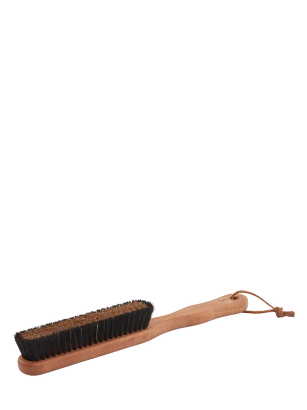 A clothing brush with a wooden handle and bronze wire bristles laid out on a plain background.