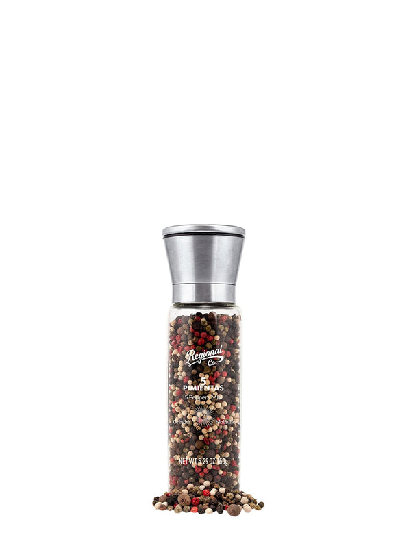 A a brushed silver metal topped glass pepper mill filled with a multicolor mix of whole peppercorns, such as rósepepper, white pepper and black pepper, with a few peppercorns spilled at the bottom against a white background.