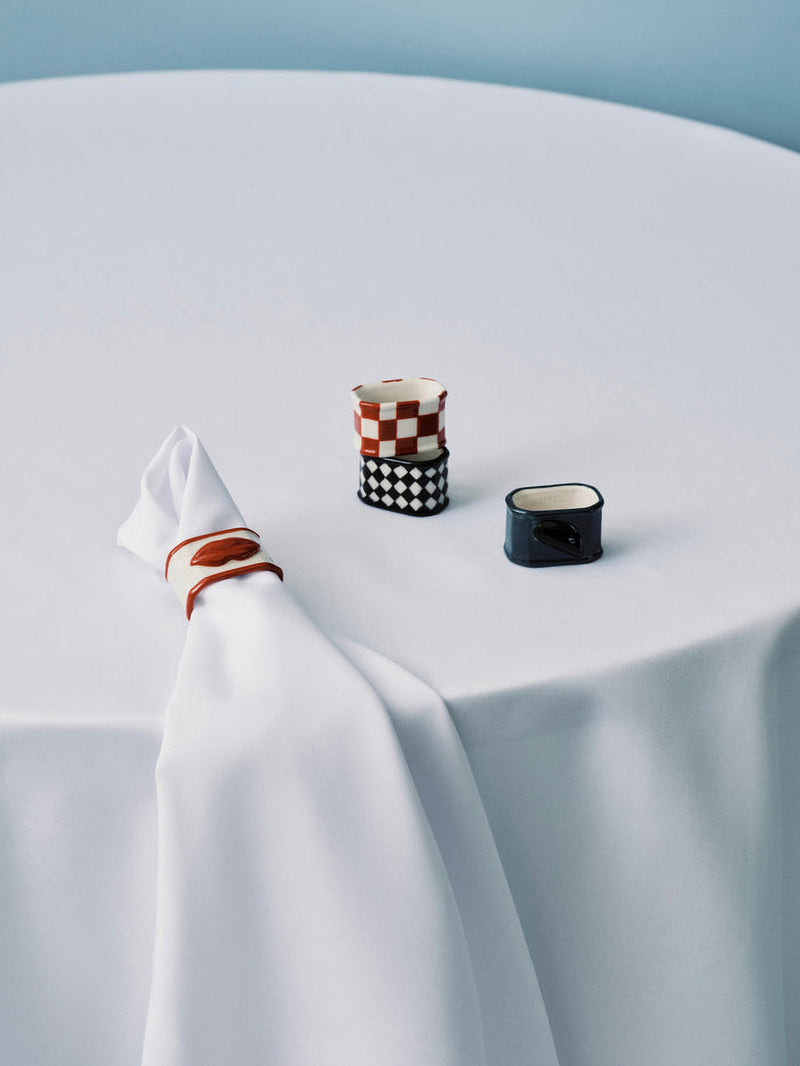 Four small ceramic napkin rings on a white table on a light blue background, white napkin on one.