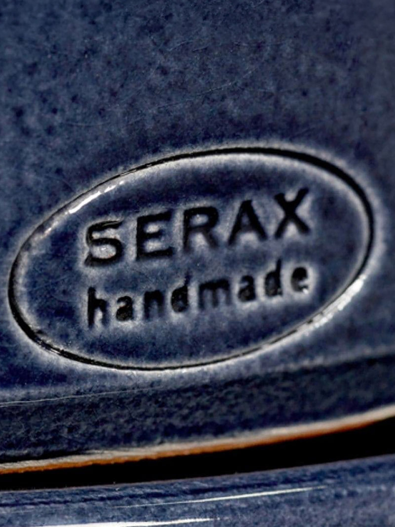 Close-up of a dark navy blue ceramic surface with an embossed oval logo reading 'SERAX handmade'.