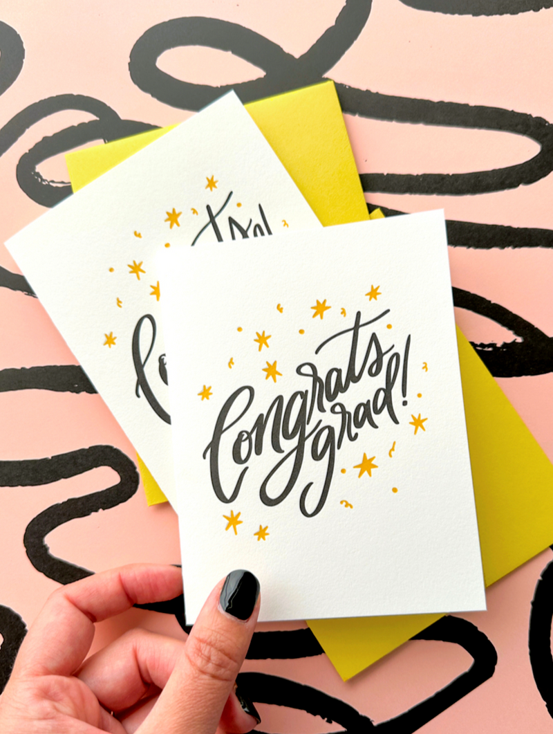 Hand holding a 'Congrats grad!' card against a colorful background