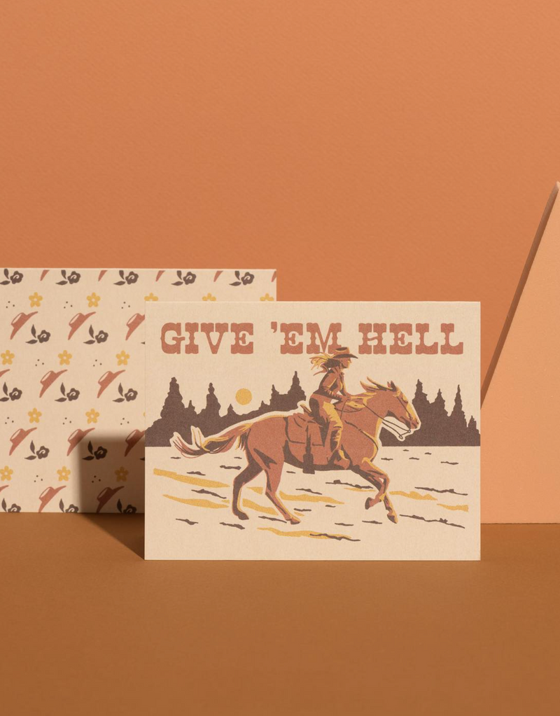 Two greeting cards on a brown background, one with a cowboy design and 'Give 'em Hell' text, the other with a pattern of arrows and stars.