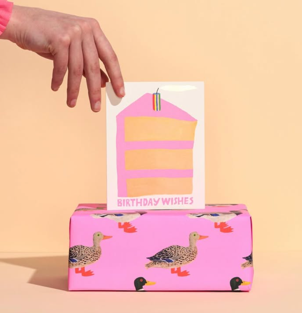 Pink gift box with duck designs and a 'Birthday Wishes' card on a beige background
